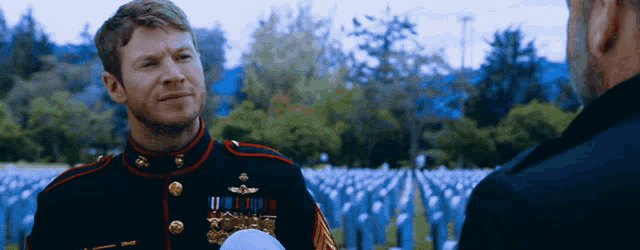 a man in a military uniform is talking to another man in front of a cemetery