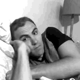 a man is laying in bed with his head on his hand and looking at the camera .