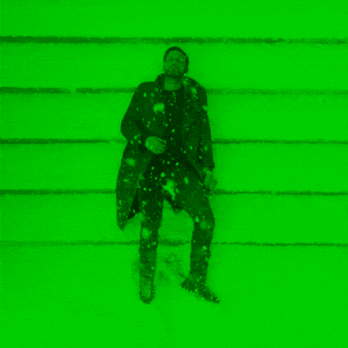 a man in a trench coat is standing in the snow in front of a green background .