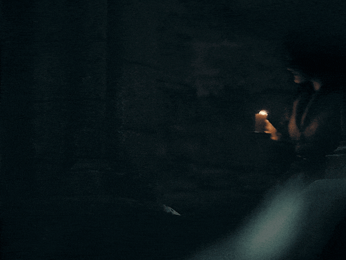 a woman is holding a lit candle in the dark