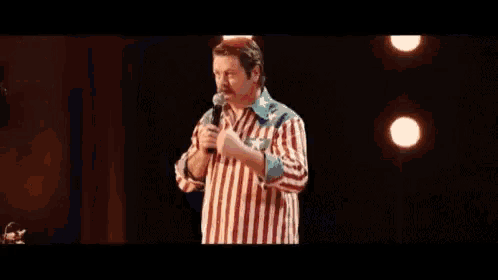 a man in a striped shirt is standing on a stage holding a microphone and dancing .