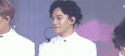 a man in a white suit with a microphone in his ear is standing in front of a group of people .