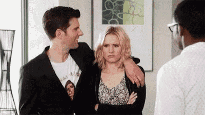 a man and a woman are standing next to each other in a living room while a man looks on .