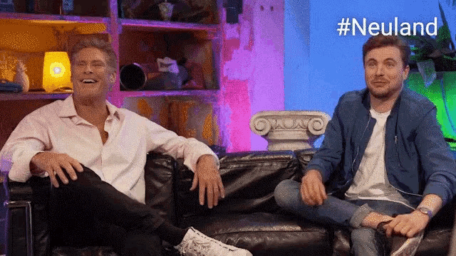 two men are sitting on a couch with the hashtag #neuland in the background