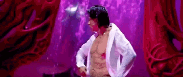 a man in a white shirt is standing in front of a purple curtain .