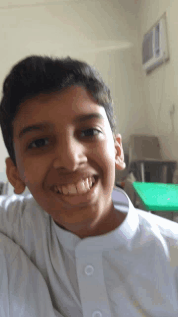 a young boy in a white shirt is smiling in front of a green table