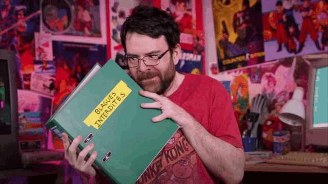 a man in a red shirt is holding a green folder with a yellow label that says " buques interdites "