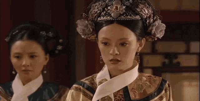two women in traditional chinese clothing are standing next to each other in a dark room .
