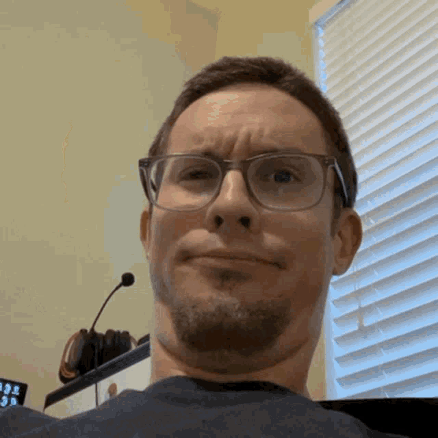 a man wearing glasses is making a funny face in front of a window