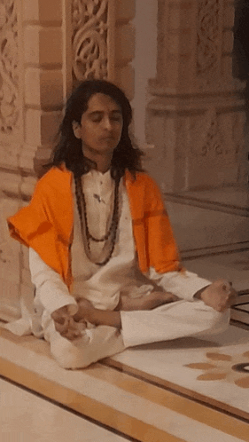 a man with long hair sits in a lotus position on the floor