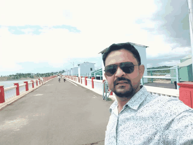 a man wearing sunglasses takes a selfie in front of a body of water