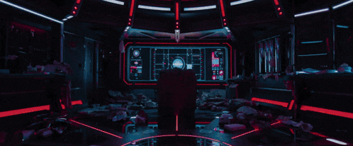 a man in a batman shirt is laying on a bed in a dark room with purple lights .