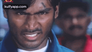 a man with a scar on his forehead is looking at the camera with another man in the background .