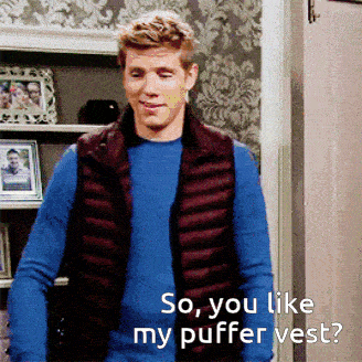 a man wearing a blue sweater and a burgundy vest is asking if he likes his puffer vest
