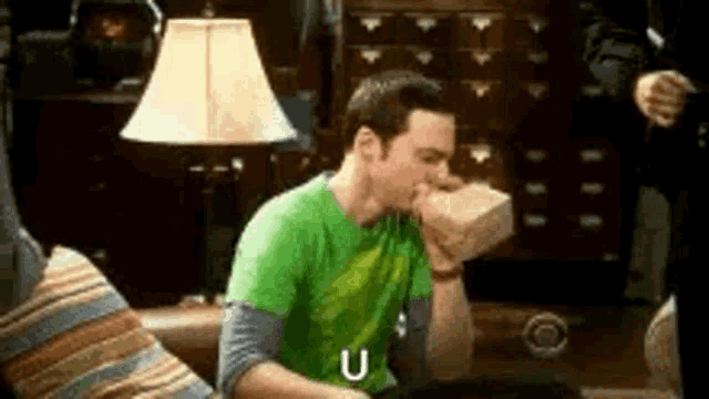 a man in a green shirt is sitting on a couch eating a piece of paper .