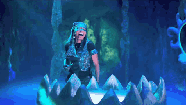 a woman in a blue costume is standing in a cave holding a sword