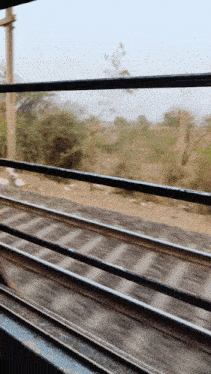 a train is going down the tracks with a fence in the foreground and trees in the background