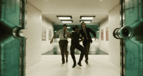 a group of people running through a hallway with a green door in the background