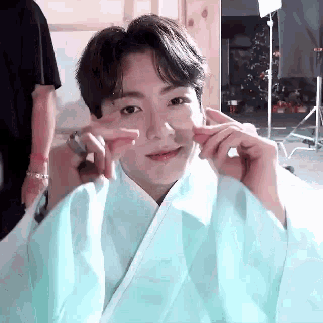 a young man is wearing a blue kimono and making a peace sign with his hands .
