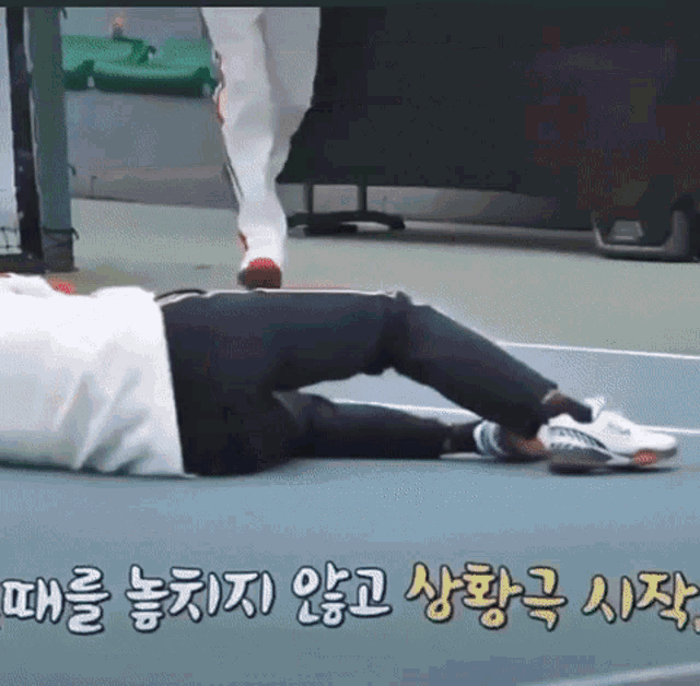 a person is laying on the ground on a tennis court with korean writing .