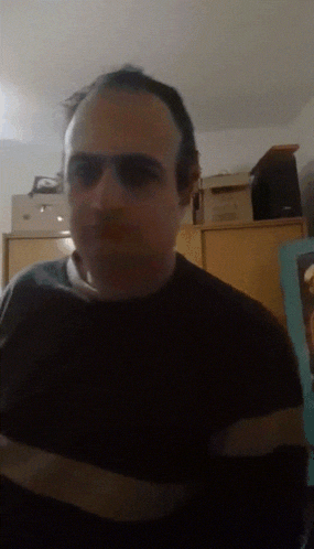 a man wearing glasses and a black shirt is standing in front of a dresser