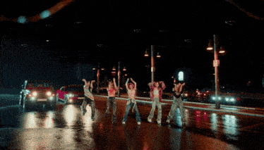 a group of women are dancing on a street at night