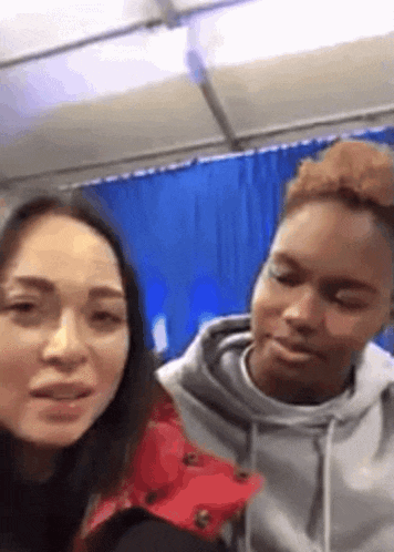 two women are standing next to each other in front of a blue curtain in a room .