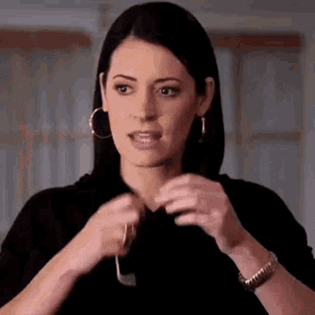 a woman wearing hoop earrings and a watch is holding a pair of glasses in her hands .