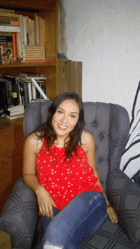 a woman in a red shirt sits in a chair in front of a bookshelf