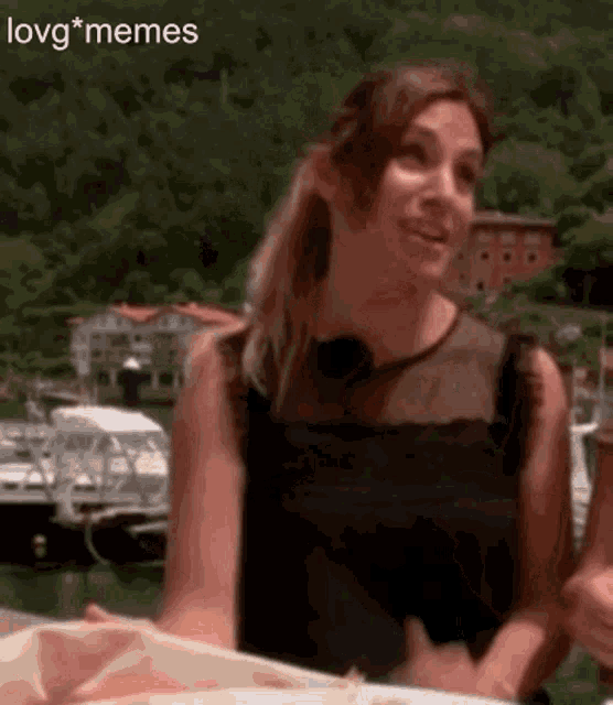 a woman in a black dress is smiling in front of a body of water with boats in the background