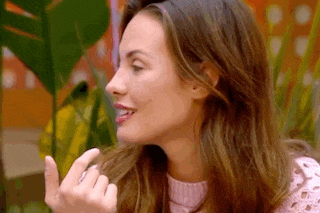 a woman in a pink sweater is making a funny face and giving a middle finger .