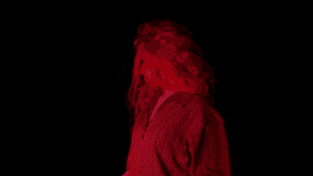 a woman with long red hair is standing in a dark room with red lights behind her .