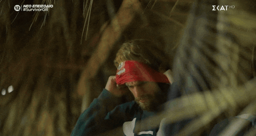 a man covering his eyes with a red bandana with the word survivor on the bottom