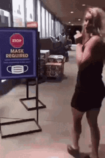 a woman is standing in front of a sign that says mask required