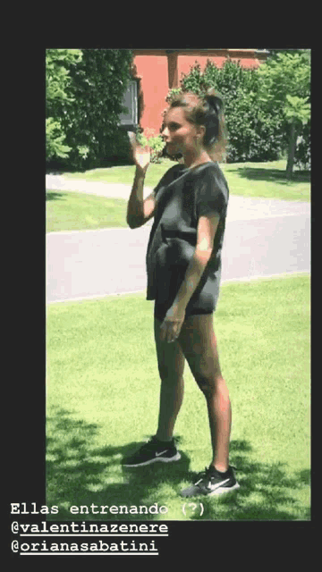 a woman in a black shirt and black shorts is standing on a lush green lawn