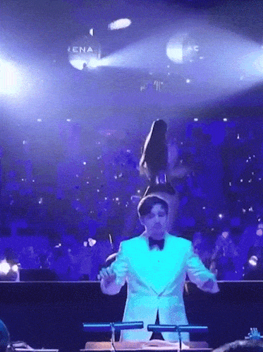 a man in a white tuxedo is leading an orchestra on stage