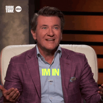 a man in a purple suit is sitting in a chair with the word im in written on his shirt