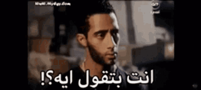 a man with a beard is looking at the camera with arabic writing on the screen behind him .