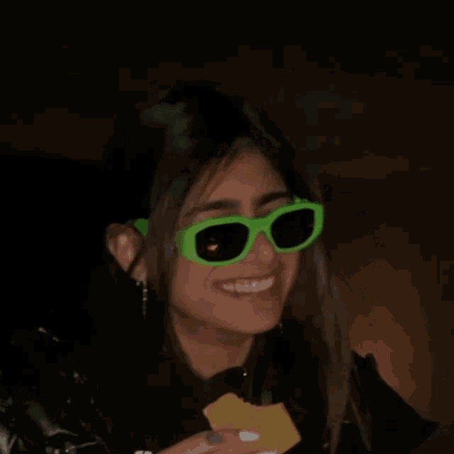 a woman wearing green sunglasses is smiling and holding a piece of s'mores