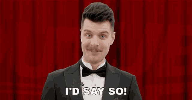 a man in a tuxedo and bow tie is standing in front of a red curtain .