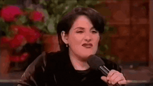 a woman is holding a microphone and talking into it while sitting in front of flowers .