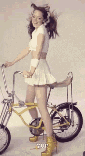 a woman in a white skirt is riding a yellow bicycle with yup written on the bottom