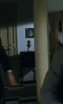 a man in a suit is standing in a dark room with a statue in the background .