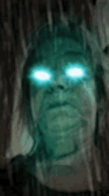 a close up of a person 's face with blue eyes glowing in the dark .