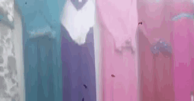 a row of pink , purple , and blue dresses are hanging on a rack .