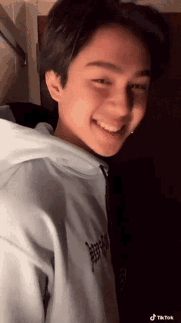 a young man wearing a blue hoodie is smiling while standing in front of a door .