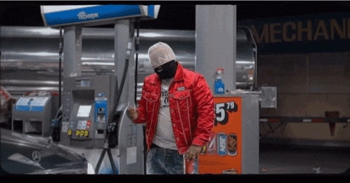 a man in a red jacket is standing in front of a gas pump that says mechanic