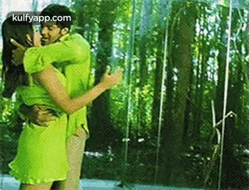 a man and woman are kissing in front of a glass wall . the woman is wearing a green dress .
