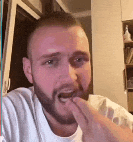 a man with a beard and a white shirt is eating something with his hands .