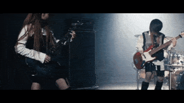 a woman playing a guitar next to a man playing a bass guitar
